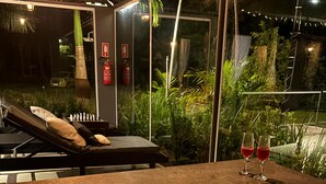 A modern outdoor hot tub area with a view of a lush garden and a chessboard on a lounge chair. - Cozy House "exclusively for Couples" Pet Friendly (Bragança Paulista)