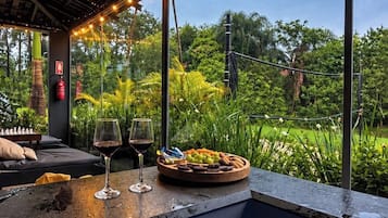 Een zwembadgedeelte met vrij uitzicht op de omgeving, een zithoek met kussens en een tafel met drankjes en fruit.