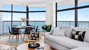Una sala de estar moderna con balcón, ventanas amplias, un sofá, una mesa de centro y un comedor con sillas y una mesa.