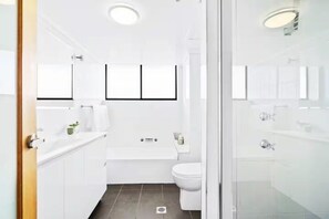 Ein modernes Badezimmer mit Badewanne, Toilette und Waschbecken. Über der Badewanne hängen drei Bilder in Rahmen.