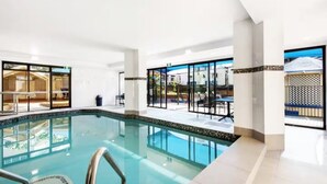 Una piscina interior moderna con paredes de vidrio transparente, suelo de baldosas y vistas al exterior.