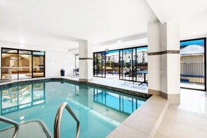 Ein moderner, überdachter Schwimmbereich mit Glaswänden, Fliesenboden und Blick ins Freie.