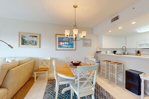 A modern kitchen with white cabinets, a wooden dining table, and a chandelier. - Oceanview Retreat w/ Balcony, Pool, & Steps from New Smyrna Beach (New Smyrna Beach)