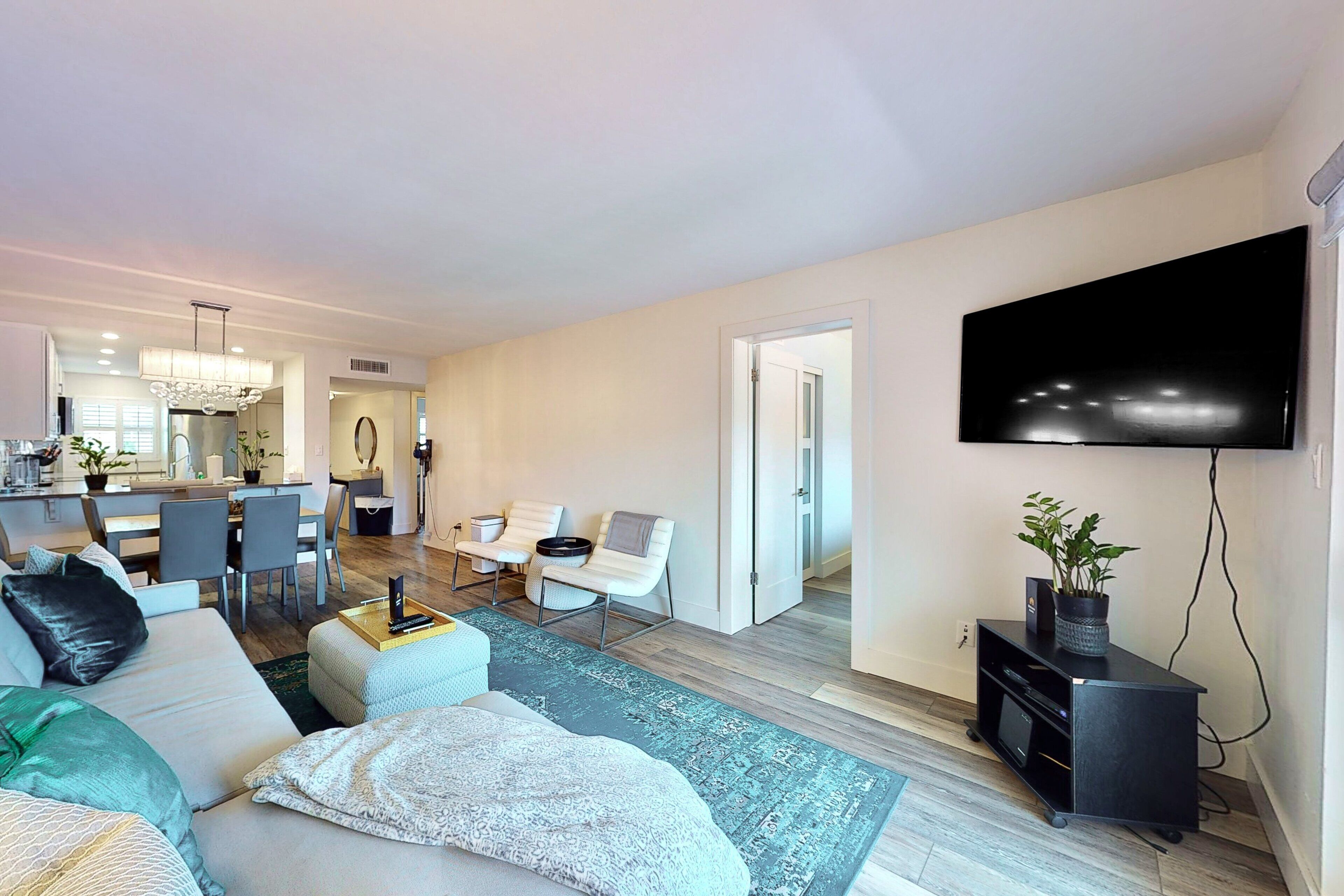 A modern living room with a sofa, chairs, a TV, and a kitchen area in the background.
