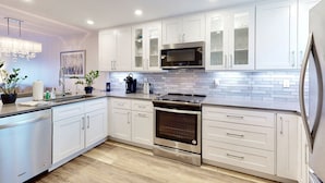 A modern kitchen with white cabinets, a stainless steel stove, and a microwave. - Modern Coastal Condo w/ Balcony, Pool & Easy Walk to the Beach (New Smyrna Beach)