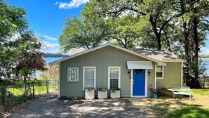 A small, single-story building with a blue door, a sign that reads 'LIVE LOVE LAKE,' and a bench in front. - Dock & Fire Pit: Lakefront Cedar Creek Home! (Mabank)