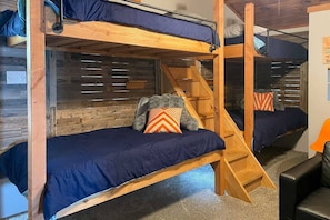 A bunk bed room with a wooden ladder, a teddy bear on one bed, and a chair in the corner.