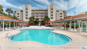 Ein Pool mit Liegestühlen und Sonnenschirmen, umgeben von einem Gebäude mit mehreren Etagen und Balkonen.