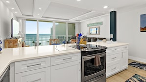 Una cocina moderna con armarios blancos, una isla grande y vistas al océano.