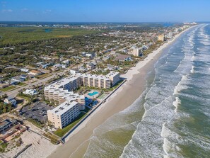An aerial view of a coastal hotel with multiple buildings, a beach, and a bridge in the background. - Relaxing Oceanfront Escape with Pools & Private Balcony Views (New Smyrna Beach)