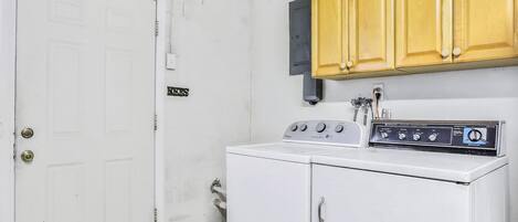 Un lavadero con lavadora blanca, armarios de madera y una puerta blanca.