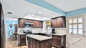 A kitchen with dark wooden cabinets, a granite countertop, and a white door with a window. - Quiet 4BR Getaway w/Private Pool, Walk to Beach & Florida Room (Ormond Beach)