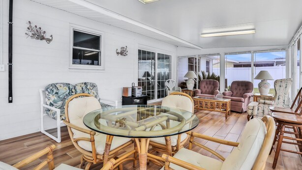 A spacious living area with a glass-top round table surrounded by wicker chairs, a large window with a view, and a cozy seating arrangement with a sofa and armchairs. - Quiet 4BR Getaway w/Private Pool, Walk to Beach & Florida Room (Ormond Beach)