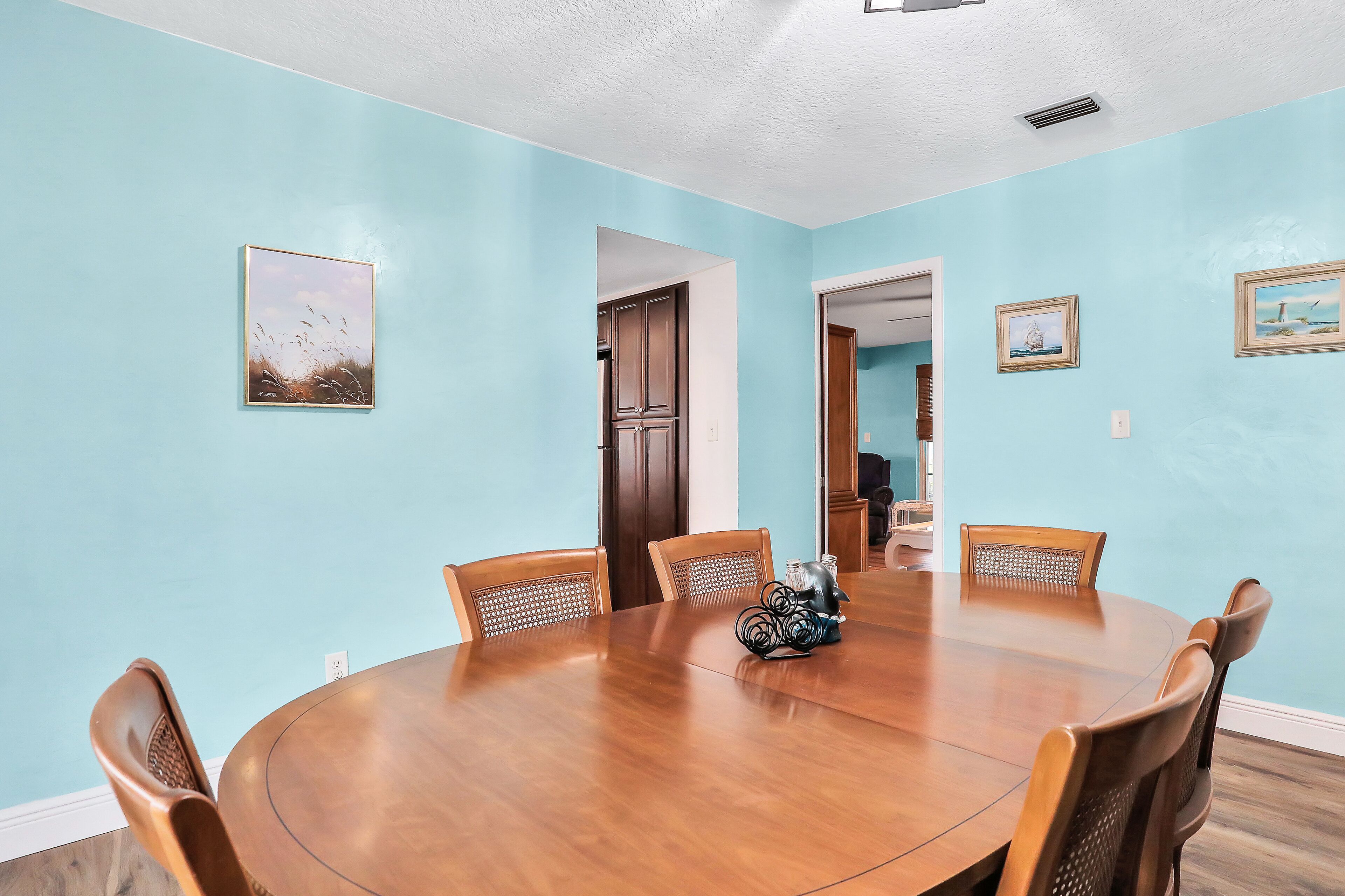 A dining room with a wooden table and chairs, light blue walls, and framed artwork.
