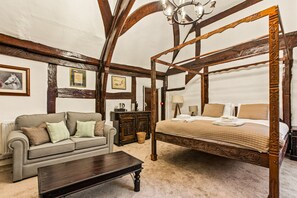 A traditional four-poster bed with a wooden frame and a canopy, a grey sofa with cushions, a wooden dresser, and a chandelier. - The George Inn Hotel Rooms (Great Missenden)