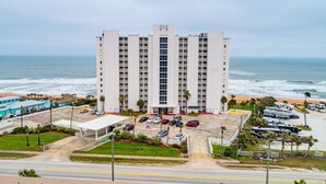 Un hotel alto con entrada central, estacionamiento y vista al mar.