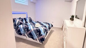 Ein Schlafzimmer mit Bett, Kommode, Spiegel und einem Fenster mit Jalousien.