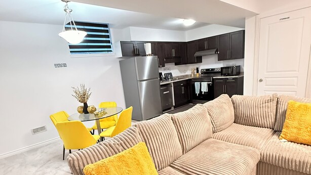 Ein modernes Wohnzimmer mit einem beigefarbenen Ecksofa, gelben Sessel und einer Küche im Hintergrund.