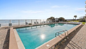 A rectangular pool with clear blue water, surrounded by a brick deck and a metal railing.