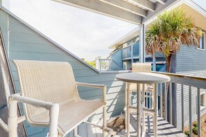 Un balcon avec une chaise et une table blanches, un palmier et, au fond, un immeuble bleu.
