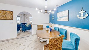 Un coin repas avec une table ronde, des chaises à revêtement bleu, un luminaire suspendu et des éléments de décoration murale sur le thème de la marine.