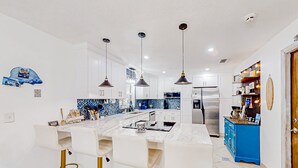 Une cuisine moderne avec des armoires blanches, un îlot en marbre et des tabourets de bar dorés.