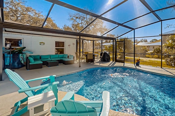 Enjoy this bright, beach-inspired pool area with comfy seating, dining space, and a sparkling screened-in pool—perfect for relaxing, entertaining, and soaking up the sunshine during your beach stay.