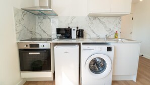 A compact kitchen with a built-in oven, microwave, and washing machine, featuring marble backsplash and white cabinetry. - Centra High Road (London)