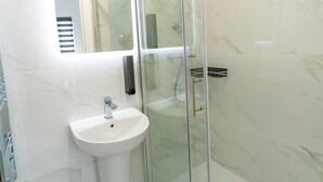 A modern bathroom with a glass shower enclosure, a white sink, and a mirror above the sink. - Centra High Road (London)
