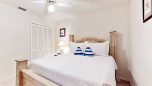 A bedroom with a wooden bed, white bedding, a ceiling fan, a nightstand, a lamp, and a framed picture on the wall. - Quiet 2-Story Getaway w/ Pool, Loft & Grill Near Daytona (Port Orange)