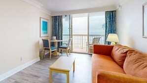 A hotel room with a balcony, a sofa, a table, and two chairs. - Oceanfront Studio with Balcony, Resort Pools & Walkable Fun (Daytona Beach)