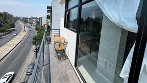 A balcony with a table and chairs, overlooking a busy street with cars and buildings. - Beautiful 2-bedroom apartment with terrace in Mexico City (Ciudad de México)