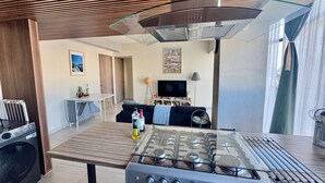 A modern kitchen with a gas stove, a dining area with a table and chairs, a sofa, and a TV in the background. - Beautiful 2-bedroom apartment with terrace in Mexico City (Ciudad de México)