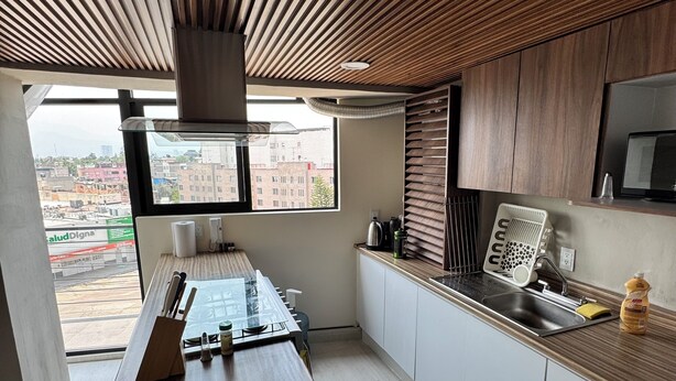 A modern kitchen with a wooden ceiling, a large window, and a view of the city. - Beautiful 2-bedroom apartment with terrace in Mexico City (Ciudad de México)