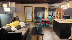 Een gezellige woonkamer met een leren bank, een eettafel met stoelen, een keukenhoek en een houten plafond.