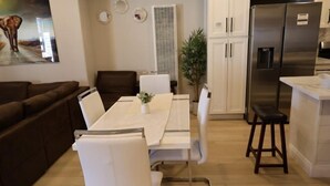 A modern living room with a dining table, white chairs, a brown sofa, a kitchen area with a refrigerator, and a potted plant. - Exotic home 3bed2bath 20min to beach downtown (La Presa)
