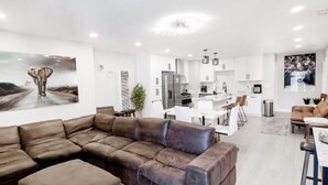 A modern living room with a sectional sofa, a dining area with a table and chairs, and a kitchen in the background. - Exotic home 3bed2bath 20min to beach downtown (La Presa)