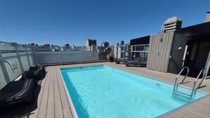 A rooftop pool with wooden deck, lounge chairs, and a city skyline view. - Excellent apartment in building with amenities. In front of Abasto Shopping Mall (Buenos Aires)
