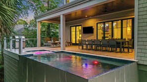 Zona de piscina exterior con terraza cubierta, sillas de descanso y una mesa de comedor.