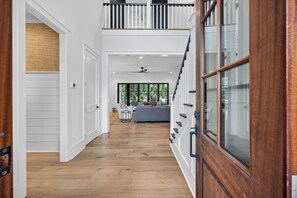 Un pasillo amplio con piso de madera, paredes blancas y una puerta de cristal que da a un balcón.