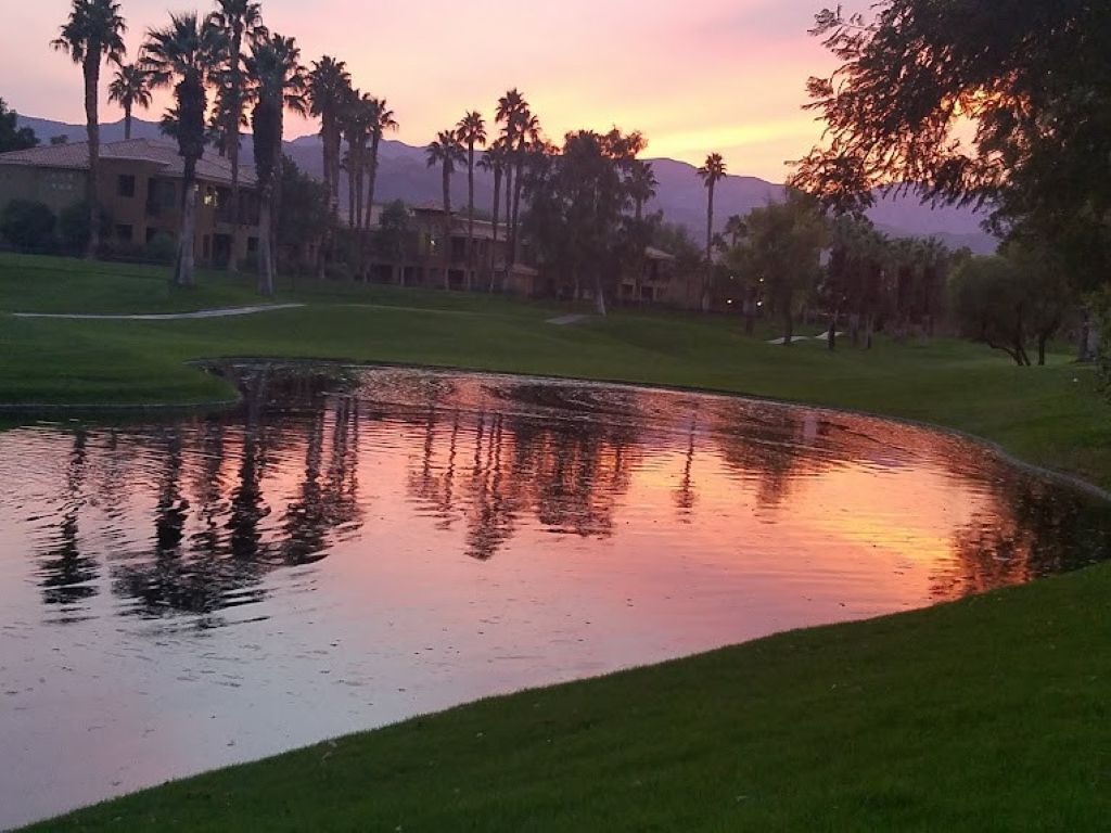 A golf course with a pond reflecting palm trees and a building in the background.