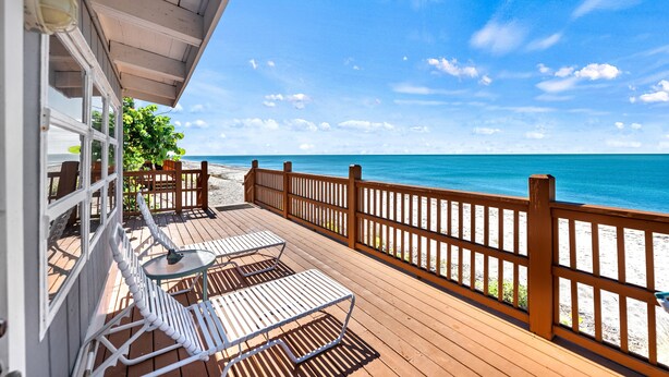 A wooden deck with white metal chairs and a table, overlooking a beach with a wooden fence. - Gulf View Escape on the Beach with Lounging Deck (Englewood)