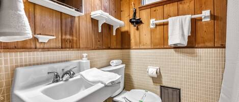 A bathroom with wooden paneling, a white sink, a toilet, and a window above the mirror.