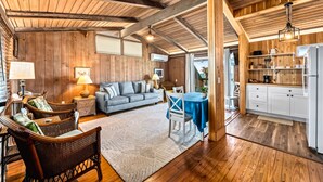 A cozy room with a wooden ceiling, a sofa, a dining table with chairs, and a kitchen area with cabinets and shelves. - Beach Front Escape with Private Balcony & Beach Access, Pet Friendly (Englewood)