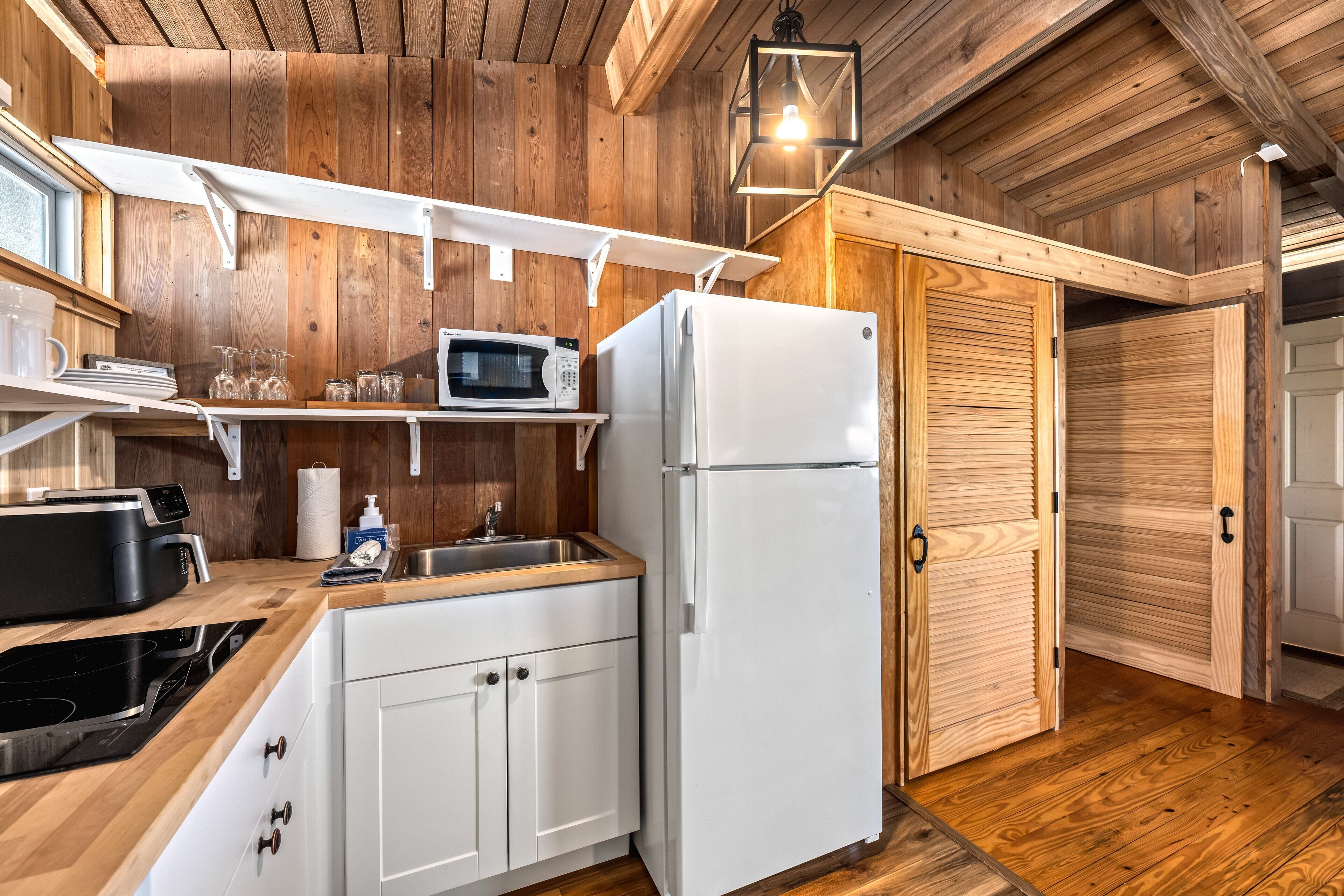 A compact kitchen with wooden walls, a white refrigerator, a microwave, and a sink.