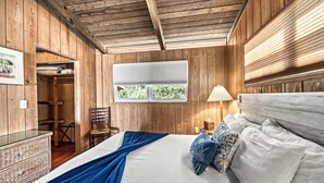 Una habitación con paneles de madera, una cama, una silla, un aparador y un ventanal.