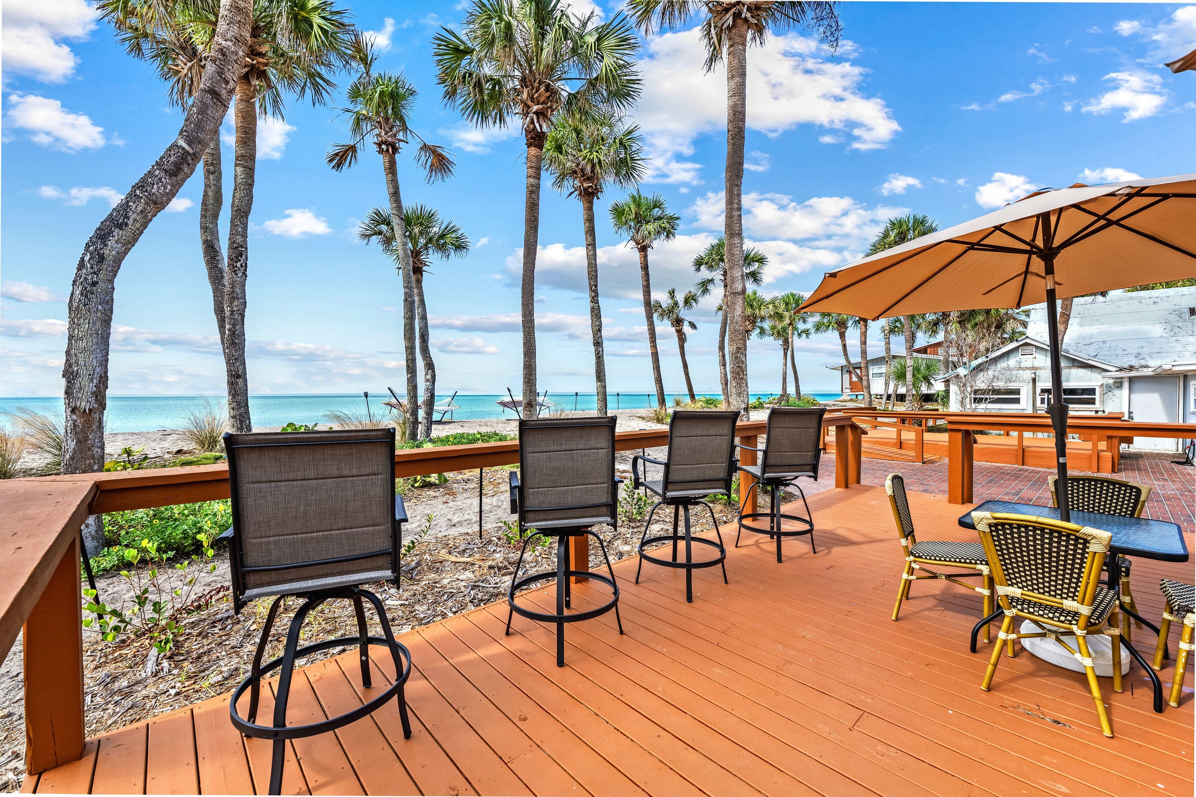 A wooden deck with outdoor seating, palm trees, and a view of the ocean.