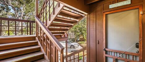 A wooden staircase leading to a porch with a view of a car parked outside.