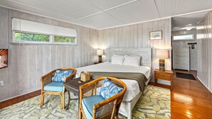 Un dormitorio con cama, dos sillones de mimbre, una mesita de noche, una lámpara, un aparador y una ventana con persianas.