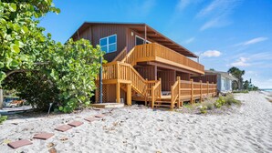 Una casa frente a la playa con un muelle de madera y escaleras que conducen a un balcón.